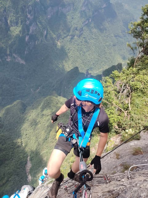 Calvin in a blue helmet and harness on a via ferrata above a green mountain valley