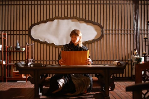 Calvin in traditional Chinese costume reading a bamboo scroll at a wooden desk